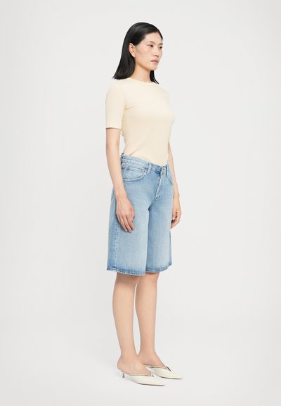 T-shirt ajusté beige clair, associé à un short en denim bleu clair arrivant au genou. Texture lisse, finition à l'ourlet brut, et poches avant visibles.