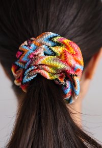 Pătură colorată cu un model în zigzag, în nuanțe vibrante de roz, albastru, portocaliu și verde, realizată dintr-un material moale și texturat.