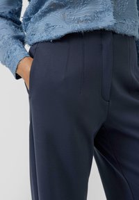 Granatowe spodnie o gładkiej fakturze, z dopasowanym krojem i plisowaniem z przodu. Boczne kieszenie bez zdobień.