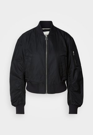 Must musternahk, mis on valmistatud siledast kangast, millel on lukuga esitasku, ribiga käised ning lühikese kujuga disain, millel on varrukatel peened volangid.