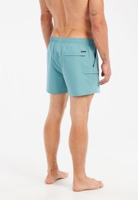 Tyrkysové plavky s elastickým pásom, dvomi zadnými vreckami a hladkým materiálom, navrhnuté pre pohodlie a flexibilitu.