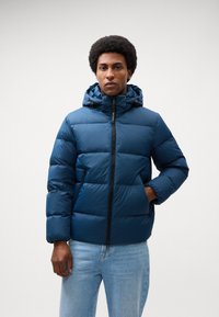 Jachetă puffer de culoare bleumarin cu închidere prin fermoar, bretele elastice la manșete și capotă. Fabricată dintr-un material neted, ușor, cu un design matlasat pentru izolație.