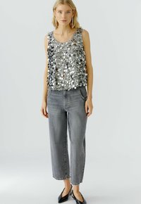 Silberner Paillettenoberteil mit rundem Halsausschnitt, kombiniert mit hoch taillierten, hellgrauen, weit geschnittenen Jeans. Das Outfit wird durch schwarze Ballerinas ergänzt.