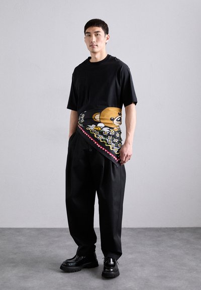 Black short-sleeve t-shirt featuring a colorful bear graphic and floral pattern on one side, paired with loose black pants and chunky black shoes.