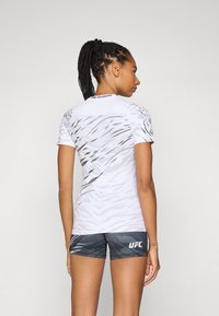 T-shirt de sport à manches courtes blanc avec un motif abstrait gris, associé à un short gris arborant un logo "UFC". Tissu lisse et léger.