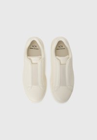 Bijele slip-on tenisice od glatkog, teksturiranog materijala s elastičnim bočnim panelima za prilagodbu. Sadrže logotip na ulošcima.