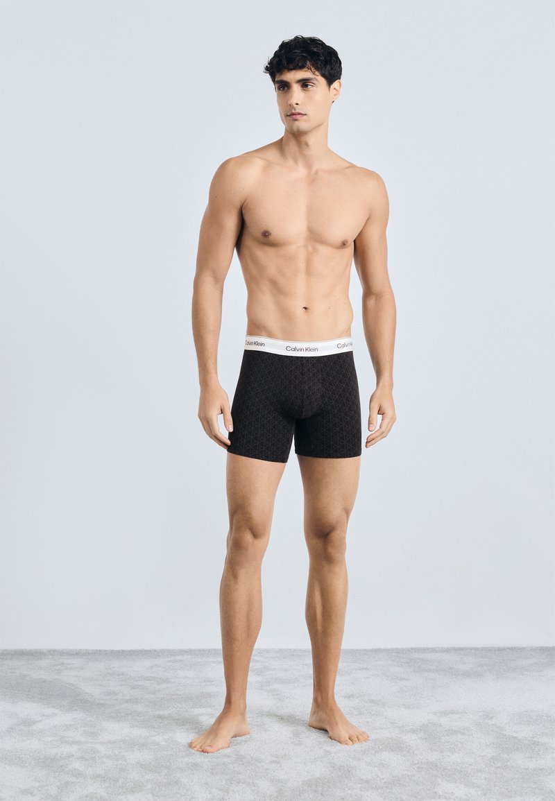 Fekete mintás boxer alsónadrág fehér Calvin Klein logóval ellátott derékrészen. Az anyag sima, szorosan illeszkedik a testhez.