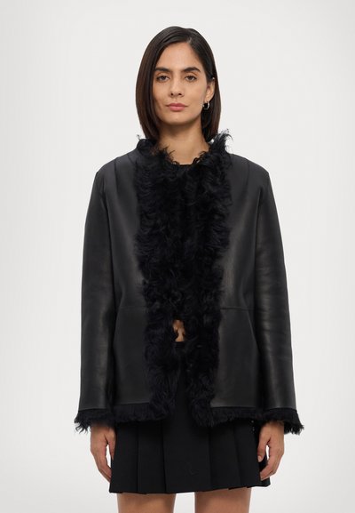 Black leather jacket featuring a curly fur trim along the collar and edges. The design is open-front with a boxy silhouette and raw hems.