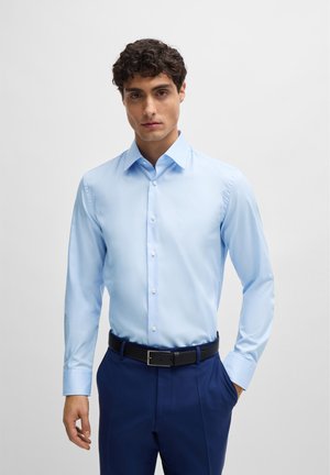 Lichtblauwe blouse met lange mouwen, een puntige kraag, een knoopsluiting aan de voorkant en een gladde textuur, gecombineerd met donkerblauwe broek en een zwarte riem.
