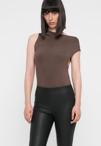 Bodysuit marron ajusté avec une épaule, bord non fini et découpe. Associé à un legging noir brillant taille haute.