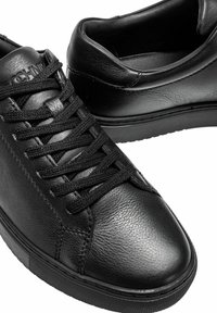 Czarne sneakersy wykonane z teksturowanej skóry, z okrągłym noskiem, płaskimi czarnymi sznurowadłami oraz gumową podeszwą z subtelnym logo na języku.