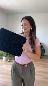 Svart quilted laptop sleeve med en fold-over klaff, med et teksturert mønster og glatt finish. Vesken blir holdt av en person.