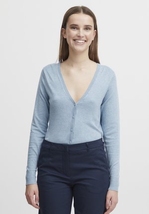 Cardigan bleu clair en tissu doux, avec un décolleté en V profond, une fermeture à boutons sur le devant et des manches longues. Associé à un pantalon foncé.