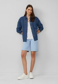 Donkerblauwe denimjacket, witte tanktop en lichtblauwe opgerolde shorts. Witte sneakers maken de outfit compleet. Glad textuur overal.