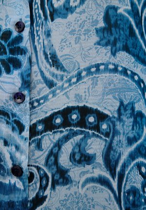 Tessuto blu a fantasia con intricati motivi floreali e paisley. Presenta tonalità di blu scuro e chiaro, e bottoni scuri. Texture liscia.