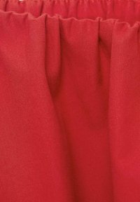 Material textil roșu cu o textură netedă, având pliuri adunate în partea de sus. Materialul pare ușor și bine finisat.