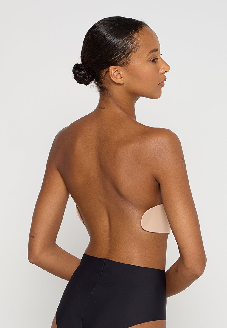 Soutien-gorge adhésif nude avec une surface lisse, une forme ergonomique et sans bretelles. Un bas taille haute noir complète le design minimaliste.