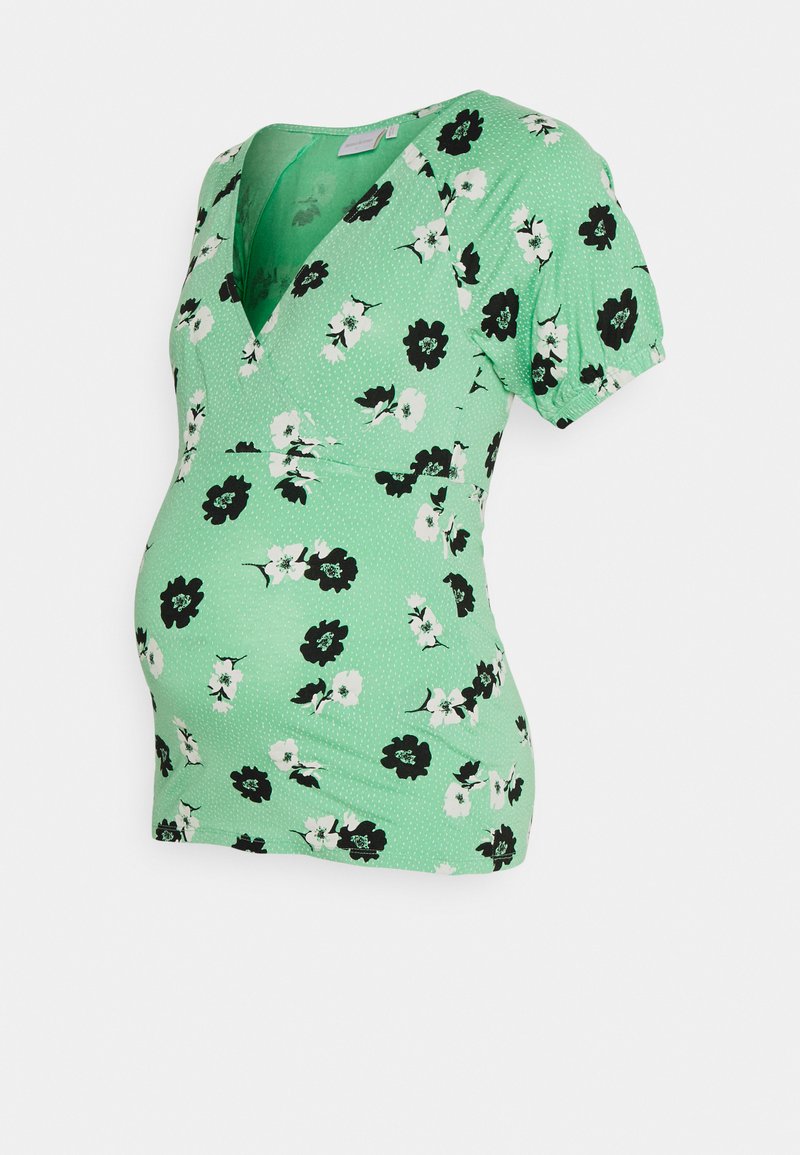 Blusa de maternidade com padrão floral em verde, decote em V, mangas curtas e efeito texturizado. Apresenta flores em preto e branco com um fundo de bolinhas.