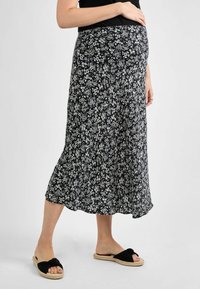Jupe de maternité noire à motifs floraux blancs, design fluide, longueur mi-mollet, texture douce, associée à des sandales à nœud noires.