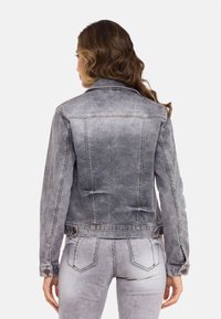Denim jack in vervaagd grijs met een klassieke kraag, knoopsluitingen en twee zijzakken. Heeft een licht verweerde textuur en een getailleerde pasvorm.