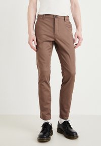 Brown slim-fit pants made of cotton blend, featuring a button closure, front pockets, and a smooth texture. Worn with black shoes.