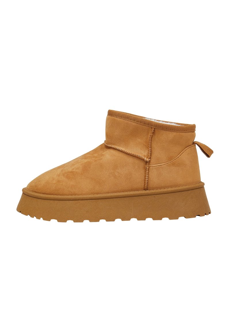 Beige Wildleder-Stiefelette mit runder Zehenpartie, strukturiertem Obermaterial, flacher Gummisohle und einer Schlaufe an der Rückseite für ein einfaches Anziehen.