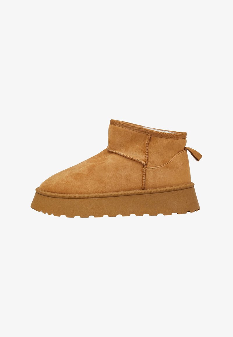 Beige Wildleder-Stiefelette mit runder Zehenpartie, strukturiertem Obermaterial, flacher Gummisohle und einer Schlaufe an der Rückseite für ein einfaches Anziehen.