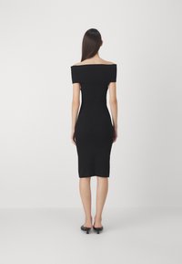 Abito nero a spalla scoperta in maglia con silhouette aderente, lunghezza al ginocchio e texture a costine. Indossato con mules nere con tacco.