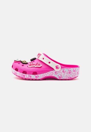 Lyserød slip-on træsko med hvid strop, Barbie logo charm og lyserød mønstret sål med flamingoer og leopardpletter.