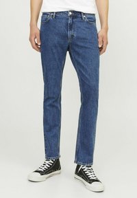 Jeans din denim albastru cu croi drept, ușor decolorate, cu buzunare frontale și închidere cu buton metalic. Compatibili cu adidași negri până la gleznă.