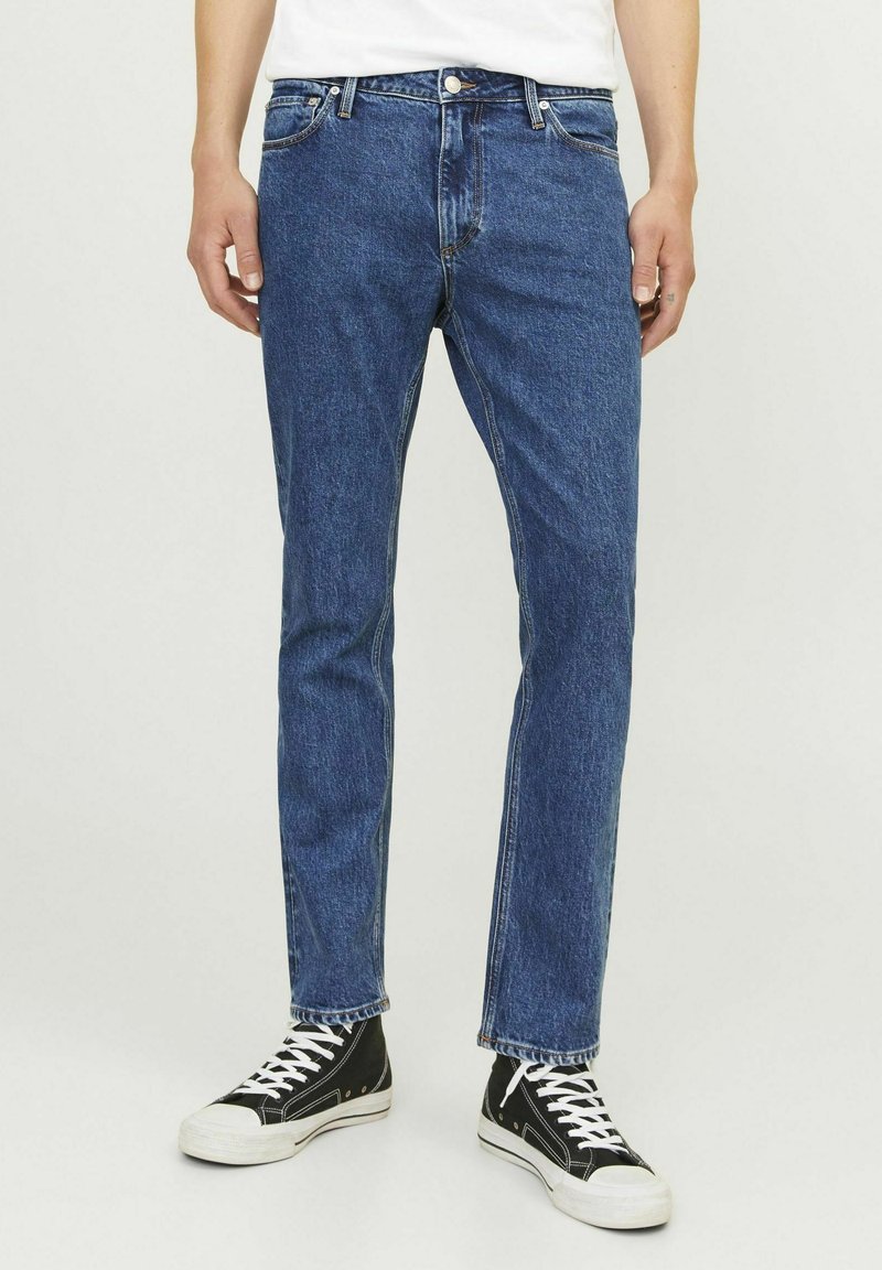 Jeans din denim albastru cu croi drept, ușor decolorate, cu buzunare frontale și închidere cu buton metalic. Compatibili cu adidași negri până la gleznă.