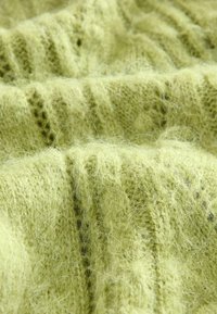 Měkká, načechraná světle zelená pletenina s viditelnými vlákny a texturovanými žebrovanými vzory zobrazená zblízka.