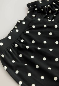 Tissu noir à pois blancs, avec une ceinture élastique froncée et une texture douce légèrement froissée.
