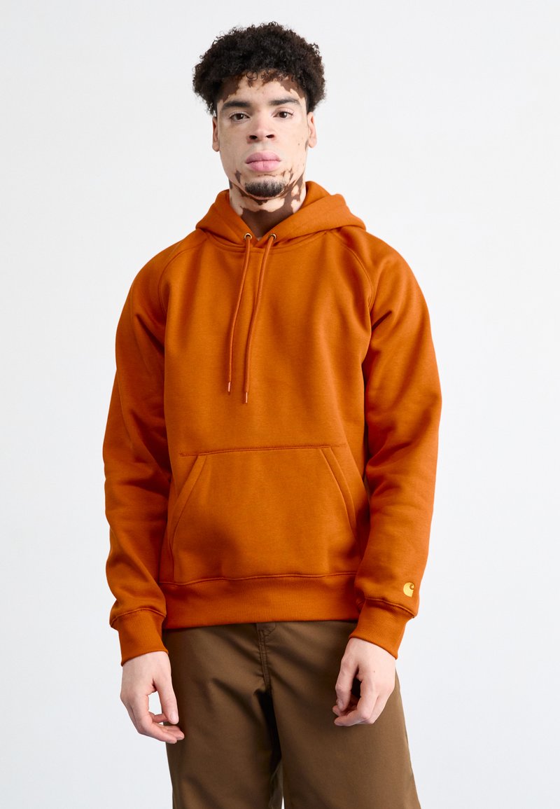 Orange hoodie with a front kangaroo pocket, drawstring hood, and ribbed cuffs. Soft fabric and logo accent on the sleeve.