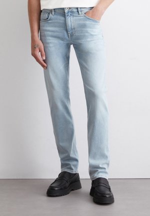 Light blue denim jeans with a slim fit, five-pocket design, and subtle fading, paired with chunky black shoes.