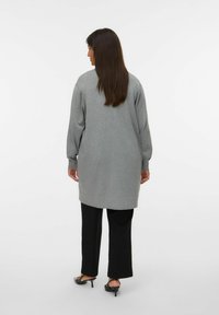 Lang grijs sweater met verlaagde schouders, ribgebreide manchetten en zoom. Gepaard met zwarte wijde broek en zwarte hakken.