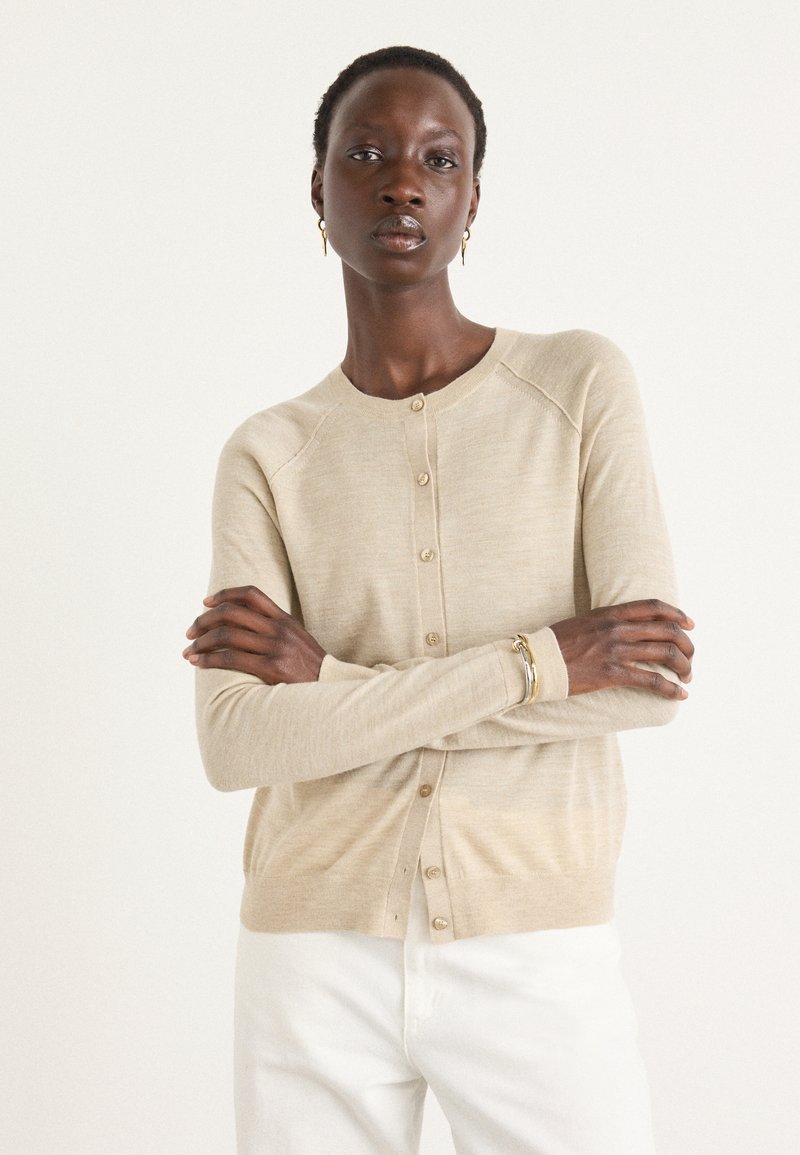 Beige stickad cardigan med rund halsringning, knäppning framtill och långa ärmar. Slät textur, ribbade detaljer och en avslappnad passform.