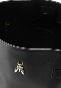 Innenraum einer schwarzen Ledertasche mit einem goldfarbenen Akzent in Insektenform. Verfügt über ein Reißverschlusstasche und eine glatte, strukturierte Oberfläche.