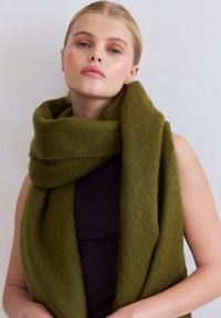 Écharpe en laine vert olive avec une texture douce et duveteuse, enroulée autour du cou. Design simple sans motifs ni éléments visibles.