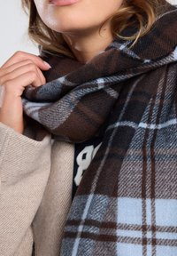 Karo-Schal in Braun-, Grau- und Hellblau-Tönen, aus weichem Stoff gefertigt, um den Hals drapiert, mit einer strukturierten Optik.