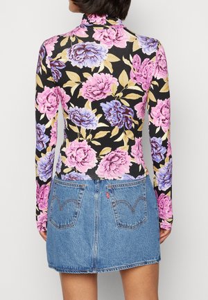 Langärmliges, tailliertes Oberteil mit schwarzem Hintergrund und großem pinken und blauen Blumenmuster, kombiniert mit einem hellblauen Jeans-Minirock mit zwei Gesäßtaschen.