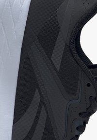 Zapatilla deportiva negra con malla texturizada y acentos suaves. Presenta una suela blanca y líneas de diseño sutiles. Cordones pasados por ojales.