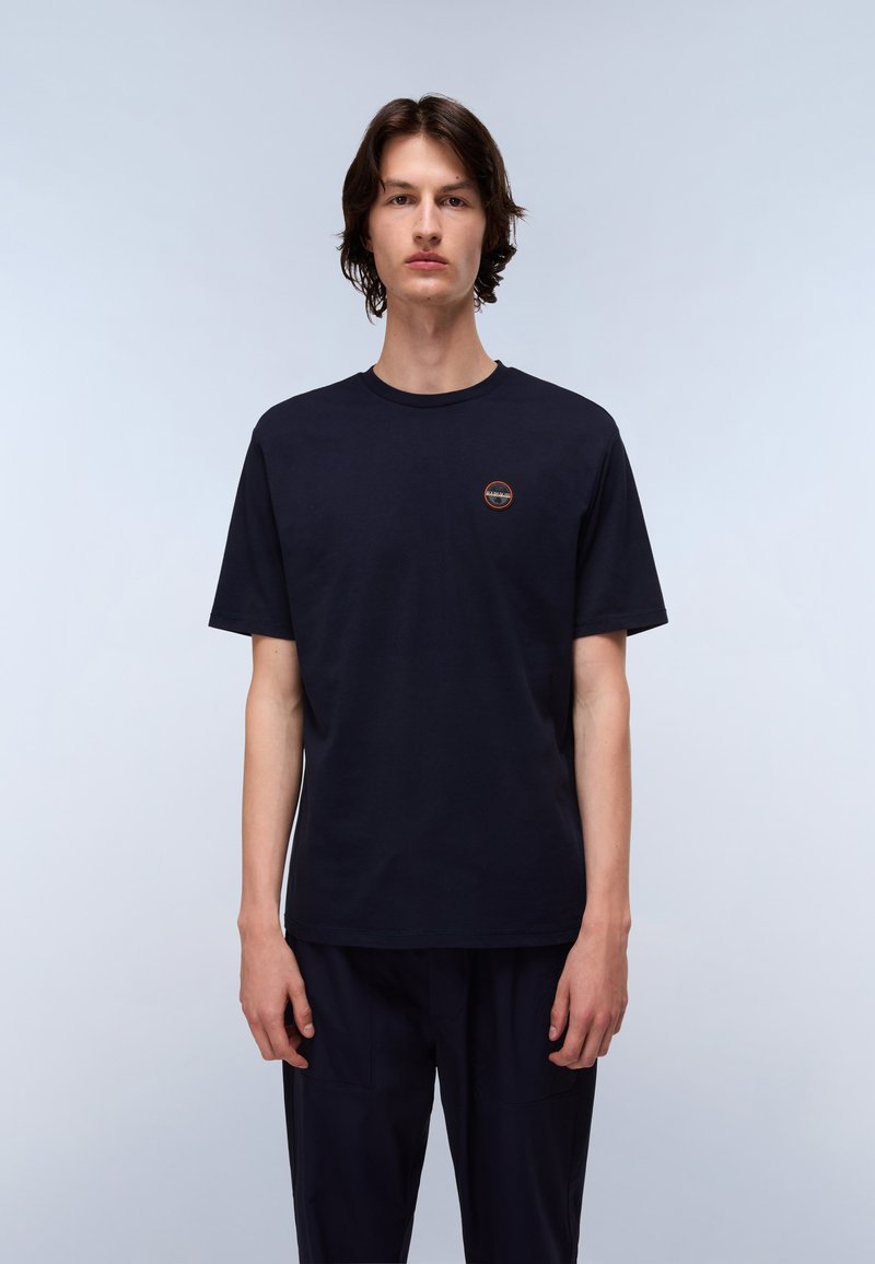 Navyblauwe katoenen T-shirt met korte mouwen, ronde crewneck en een klein rond logo-detail op de borst. Model draagt bijpassende navybroeken.