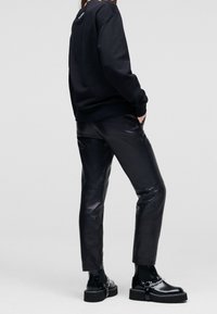 Sudadera negra con puños acanalados, combinada con pantalones de cuero negros ajustados y botas de plataforma negras chunky con acentos de cadena.