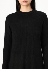 Suéter de punto ribeteado negro con escote redondo y mangas largas. La textura es suave y ligeramente peluda, con un corte holgado y relajado.