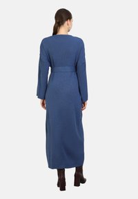 Langes, blaues, geripptes Strickkleid mit langen Ärmeln, einem Taillengürtel und gerader Silhouette, kombiniert mit braunen Blockabsatzstiefeln.