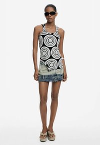 Juodos ir baltos spalvos, apskritimo rašto tankinis viršus, derinamas su džinsine mini sijonu. Modelis dėvi tamsius akinius nuo saulės ir šviesiai smėlio spalvos platforminius batus.