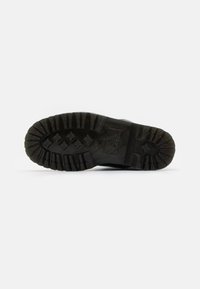 Svart gummisula med djupa mönster för grepp, med en hexagonal struktur och logotypavtryck, som ger hållbarhet och grepp.