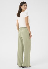 Svetlo béžové tričko s krátkymi rukávmi, kombinované s voľnými svetlozelenými širokými nohavicami s elastickým pásom. Hladká textúra látky.