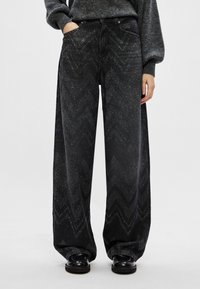 Calças jeans largas pretas com um padrão de espinha de peixe, adornadas com brilhos subtis, feitas de denim. Com um design clássico de cinco bolsos.